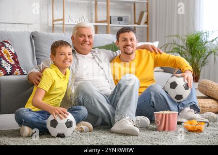 Garçon avec son père et son grand-père regardant un match de football assis sur le sol à la maison Banque D'Images
