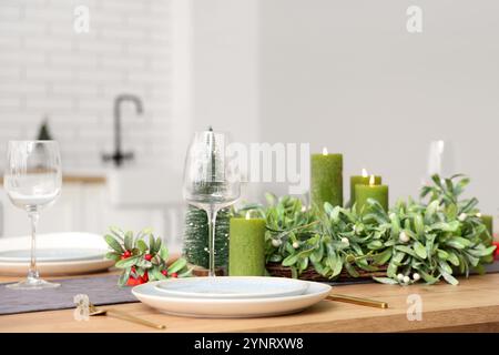 Table de Noël avec couronne de gui, bougies et verres dans la salle à manger Banque D'Images