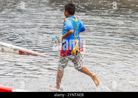 SAMUT PRAKAN, THAÏLANDE, SEP 25 2024, garçon pieds nus courant dans une flaque d'eau dans la rue Banque D'Images