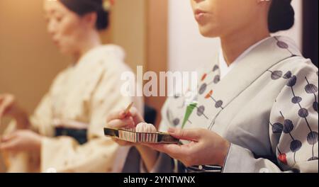 Thé, cérémonie et femmes en kimono avec des bonbons, culture alimentaire asiatique et service d'accueil en voyage. Vêtements traditionnels, wagashi et mains de fille Banque D'Images