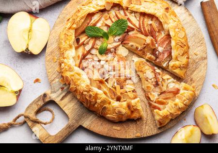 Galette de pommes fraîchement cuite décorée de flocons d'amandes et de feuilles de menthe, servie sur une planche de bois Banque D'Images