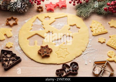 La pâte déroulée est en cours de préparation pour les biscuits de noël, avec diverses formes festives comme des maisons, des arbres, des étoiles et des flocons de neige Banque D'Images