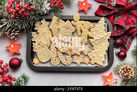 Plat de biscuits de pain d'épices de noël sur une plaque de cuisson, entouré de décorations festives et de bougies allumées, créant un SC de vacances chaleureux et accueillant Banque D'Images