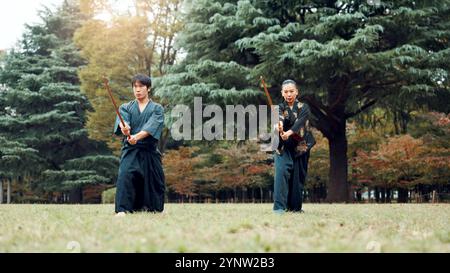 Épée, arts martiaux et personnes dans la nature s'entraînant ensemble pour l'aïkido, l'entraînement de combat ou le défi de samouraï en plein air. Guerrier, homme et femme japonais Banque D'Images