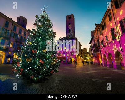 Arbre de Noël illuminé n le centre d'une place de ville pavée au crépuscule entouré de bâtiments historiques avec des projections colorées sur les murs. Banque D'Images