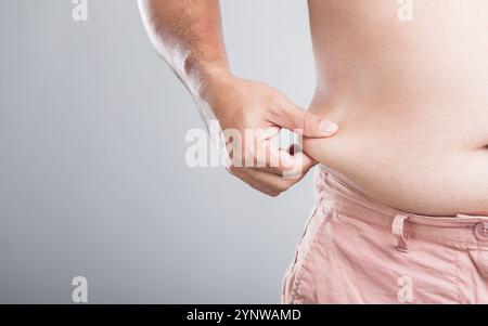 Un homme avec un plus grand physique se tient debout, tenant sa taille pour vérifier ou mesurer sa taille et la graisse abdominale, soulignant l'importance de la surveillance b Banque D'Images