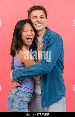 Heureux jeune couple embrassant et souriant sur un fond rose. Vertical Banque D'Images