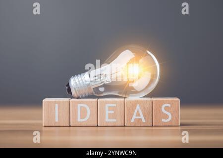 Une ampoule à côté des lettres en bois orthographiant «IDÉES» disposées sur une table symbolise l'étincelle des nouvelles idées et de la créativité. Cette image reflète inspira Banque D'Images