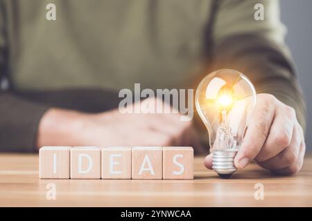 Une ampoule à côté des lettres en bois orthographiant «IDÉES» disposées sur une table symbolise l'étincelle des nouvelles idées et de la créativité. Cette image reflète inspira Banque D'Images