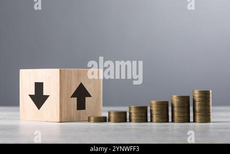 Blocs de bois avec des flèches vers le haut et vers le bas, à côté de pièces soigneusement empilées disposées du plus petit au plus grand, symbolisant les tendances financières et la croissance Banque D'Images
