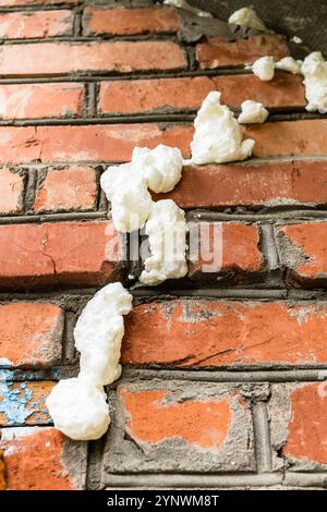 des fentes remplies de mousse de construction fraîche dans le mur de briques du hangar du village en gros plan Banque D'Images