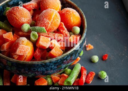 Un mélange vibrant de légumes surgelés dans un bol, mettant en valeur leurs couleurs vives sur un fond bleu profond. Banque D'Images