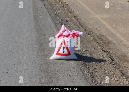 Un sac marqué d'un panneau d'avertissement se trouve au bord de la route, ce qui suggère que la prudence est nécessaire pour les véhicules qui passent et les piétons. Banque D'Images
