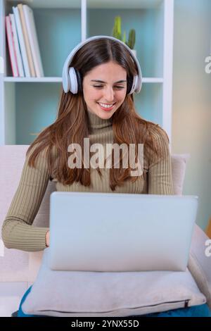 Femme souriant tout en travaillant à la maison avec des écouteurs et ordinateur portable.Interior. Banque D'Images