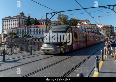 Porto, Portugal - 12 septembre 2024 : Un tramway animé traverse un pont avec des bâtiments historiques à Porto. Banque D'Images