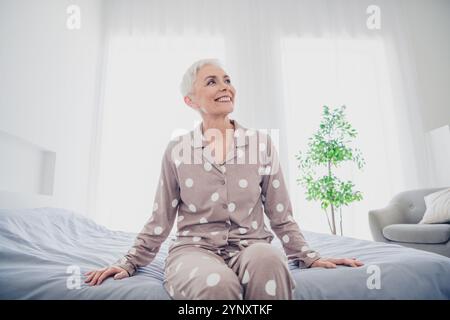 Charmante femme âgée avec les cheveux gris profitant de la lumière du matin dans une chambre confortable Banque D'Images