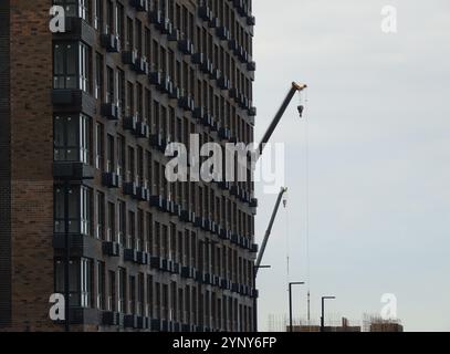 bâtiment brun à plusieurs étages en perspective linéaire avec des grues de construction dans la distance, étape finale de la construction de l'immeuble d'appartements Banque D'Images