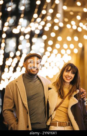 Un couple joyeux aime faire du shopping de Noël sous un auvent de lumières festives, embrassant l'esprit des fêtes ensemble. Banque D'Images