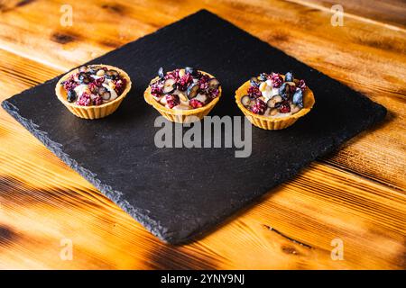 Trois tartelettes avec de la crème de fromage cottage et des myrtilles sur un panneau de mica noir sur un fond en bois. Photo de haute qualité Banque D'Images