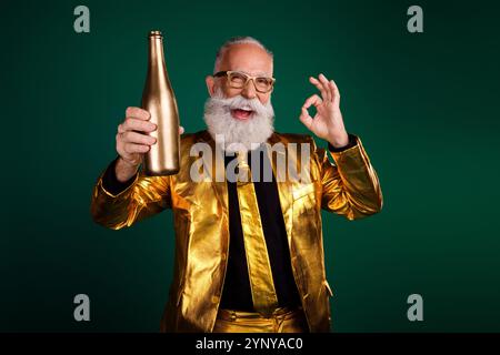 Célébrant dans le style : homme barbu mature en costume doré tenant la bouteille sur fond vert Banque D'Images