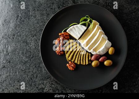 Fromage à la crème camembert avec olives, romarin et noix sur une assiette noire. Vue de dessus. Banque D'Images