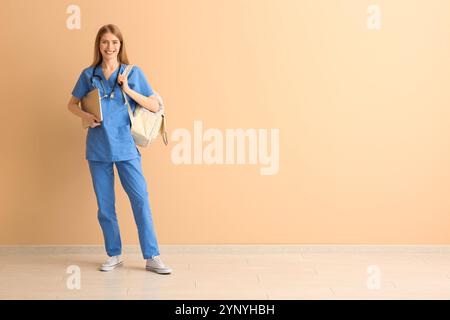 Interne médicale féminine avec ordinateur portable et sac à dos près du mur beige Banque D'Images