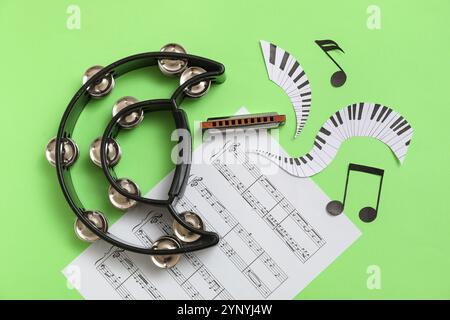 Composition avec harmonica, tambourin, feuille de musique et décor en papier sur fond vert Banque D'Images