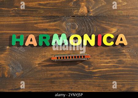 Mot HARMONICA fait de lettres colorées et instrument de musique sur fond de bois Banque D'Images