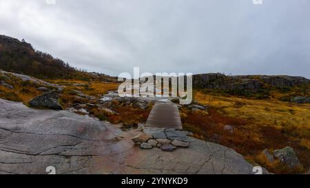 Un paysage pittoresque avec un terrain rocheux avec une passerelle en bois. La région est entourée de feuillage d'automne et de ciel nuageux, créant un an serein Banque D'Images