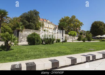 Parc paysager avec pelouse d'herbe verte et vieux bâtiment architectural jaune avec tuiles de toit en terre cuite abritant les bureaux du comté de Zadar à la fin s. Banque D'Images