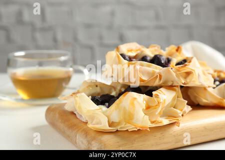 Délicieuses pâtisseries feuilletées avec des myrtilles et du thé sur une table blanche, gros plan Banque D'Images