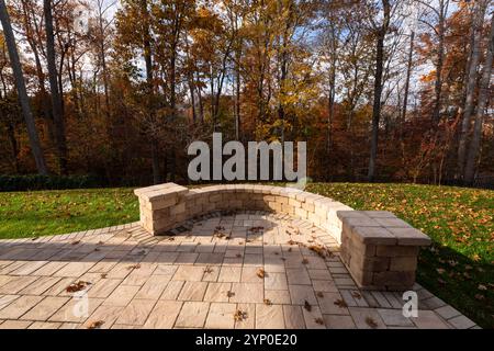 Une cour sereine avec un patio en pierre courbé entouré de feuillage d'automne vibrant, créant un espace extérieur paisible idéal pour la détente et natu Banque D'Images