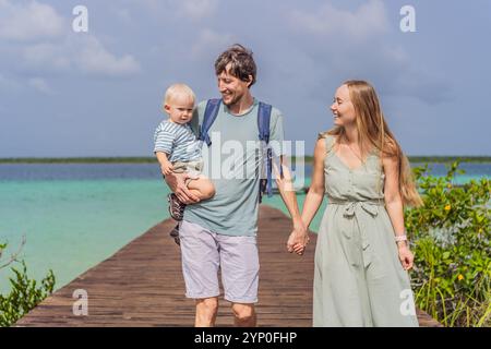 Maman, papa et leur bébé fils explorant la jetée en bois au-dessus des eaux turquoises du lac Bacalar, au Mexique. Concept de destination de voyage tropical paisible Banque D'Images