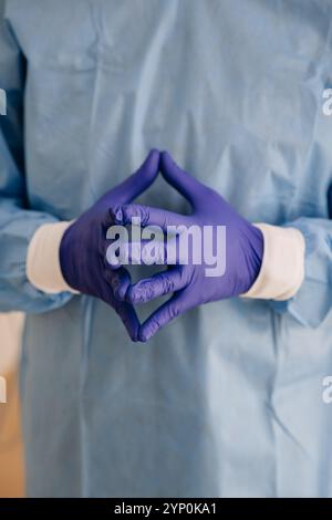 Professionnel de santé en gommage bleu avec les mains attachées portant des gants stériles Banque D'Images