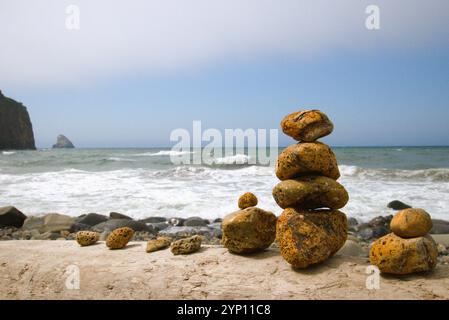 Gros plan de petites pierres orange empilées les unes sur les autres, avec des vagues coulant sur les rochers sur la plage en arrière-plan. Banque D'Images