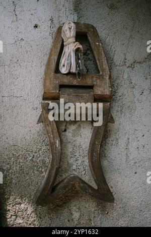 Un vieil outil en bois, probablement une pince ou une presse traditionnelle, monté sur un mur de ciment texturé, avec un tissu enroulé fixé dessus, donnant un rustique et Banque D'Images