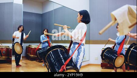 Japonais, batterie et personnes en studio pour la musique sur instrument pour la performance, la pratique ou la classe. Taiko, des femmes ou des femmes battrices apprenant dans le groupe à Banque D'Images