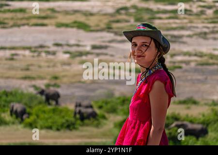 Une fille souriante dans un chapeau marchait à travers la savane sur fond d'éléphants au Kenya, en Afrique de l'est. Safari pédestre. Banque D'Images