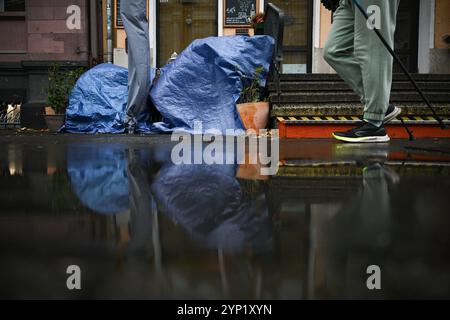 Berlin, Allemagne. 28 novembre 2024. Un homme passe devant un café fermé par temps pluvieux, devant lequel les chaises et les tables sont recouvertes d'une bâche. Crédit : Sebastian Gollnow/dpa/Alamy Live News Banque D'Images