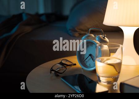 Objets personnels et lampe allumée sur la table de chevet dans la chambre, lit en arrière-plan Banque D'Images