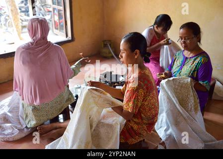 Femmes utilisant un outil semblable à un stylo (canting) pour appliquer de la cire chaude liquide dans le processus de fabrication du batik, atelier de batik Wirakuto, Pekalongan, île de Java, Indonésie Banque D'Images