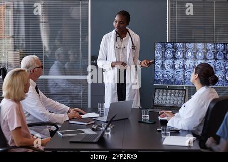 Radiologue professionnelle d'origine afro-américaine présentant les résultats de la recherche à des collègues lors d'une réunion du conseil d'administration, pointant vers l'affichage avec IRM Banque D'Images