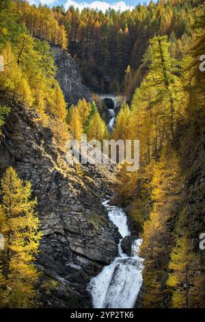 Un pont en voûte de pierre dans les Alpes françaises en automne, une cascade coulant sous la rivière Bachelard , entourée de mélèzes jaunes Banque D'Images