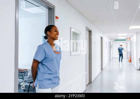 Médecin féminin heureux avec les mains derrière derrière debout sur la porte de la salle d'examen en clinique Banque D'Images