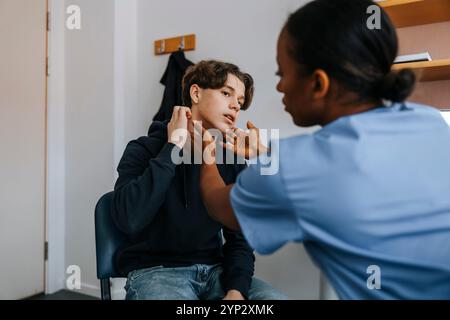Médecin féminin vérifiant le cou du patient tout en étant assis dans la salle d'examen médical Banque D'Images