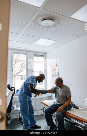 Main experte médicale masculine vérifiant le patient âgé assis sur le lit dans la salle d'examen Banque D'Images