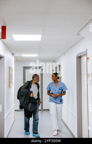 Médecin féminin discutant en marchant avec un homme âgé dans le couloir de l'hôpital Banque D'Images