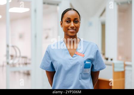 Portrait d'une femme médecin souriante dans des gommages bleus avec les mains derrière le dos à l'hôpital Banque D'Images