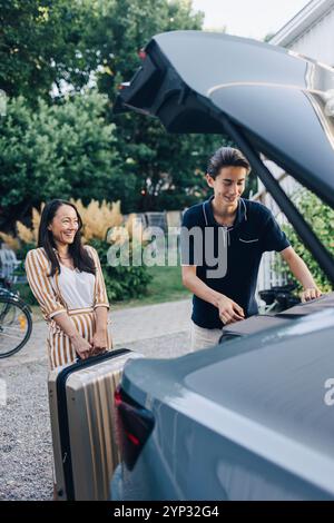 Femme heureuse aidant son fils adolescent à charger des bagages dans le coffre de la voiture Banque D'Images