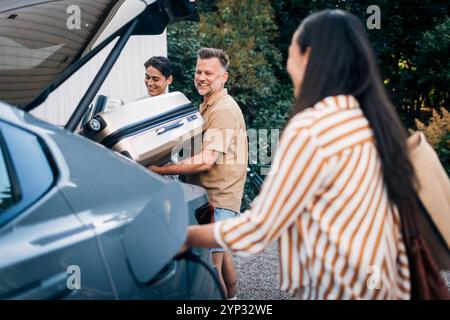 Vue arrière de la femme chargeant la voiture tandis que l'homme heureux chargeant les bagages avec le fils dans le coffre Banque D'Images